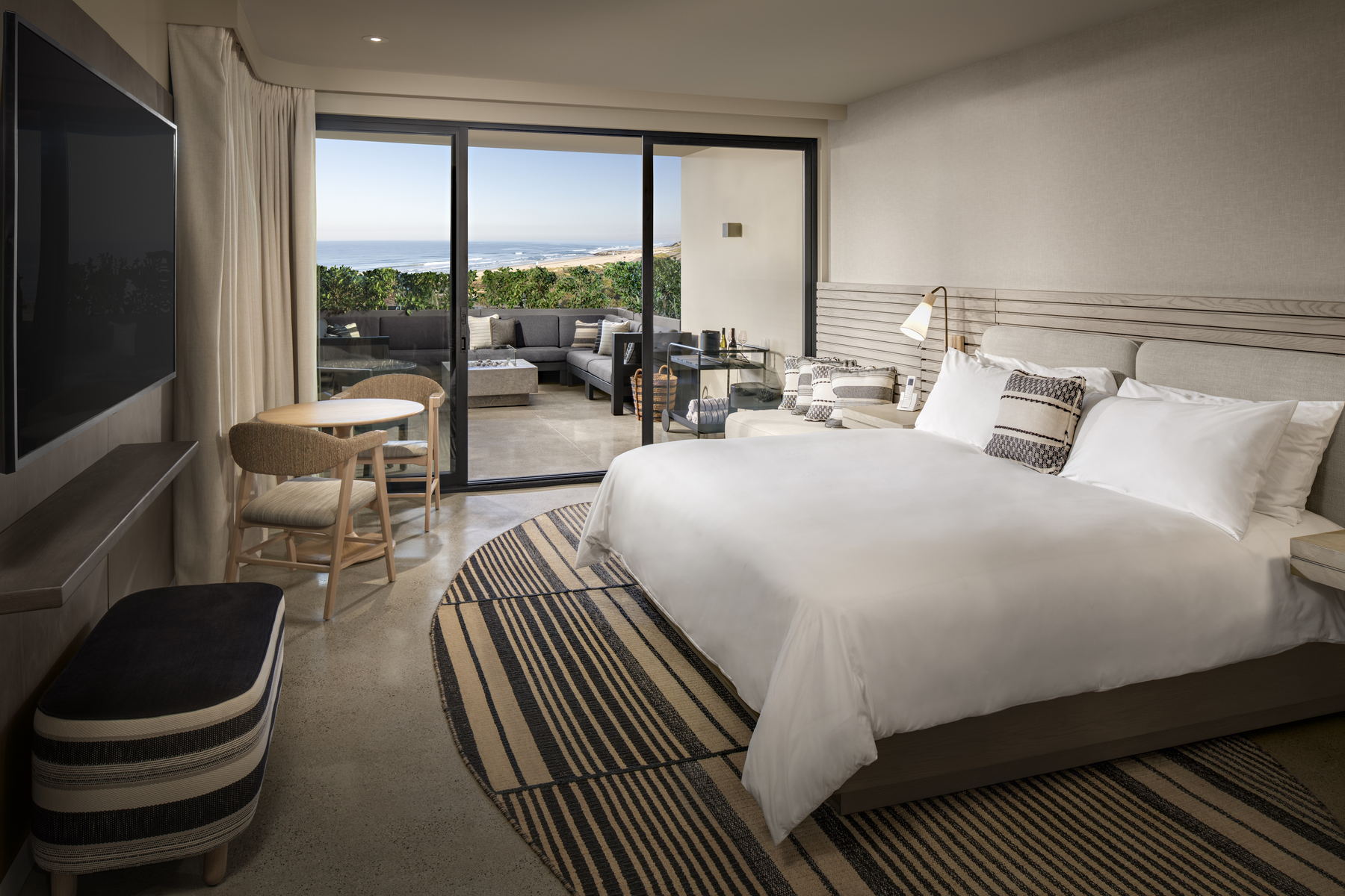 Ocean view king room with a low platform bed, woven rug, and sliding doors open to a balcony overlooking the sea
