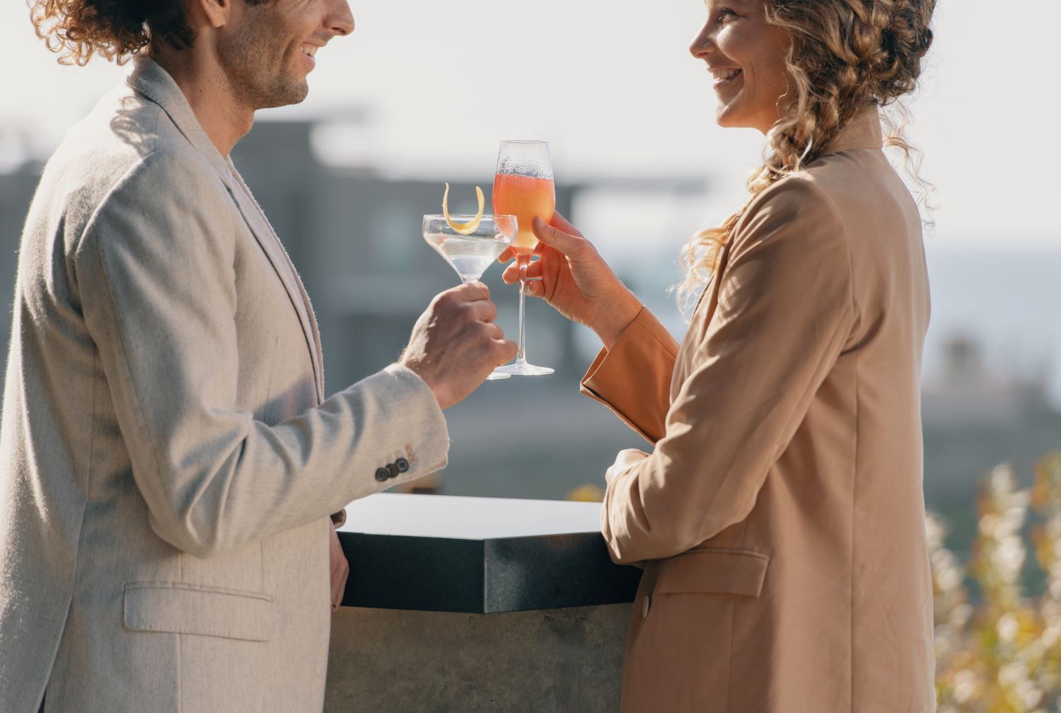 Two people touching glasses on a terrace in late afternoon light
